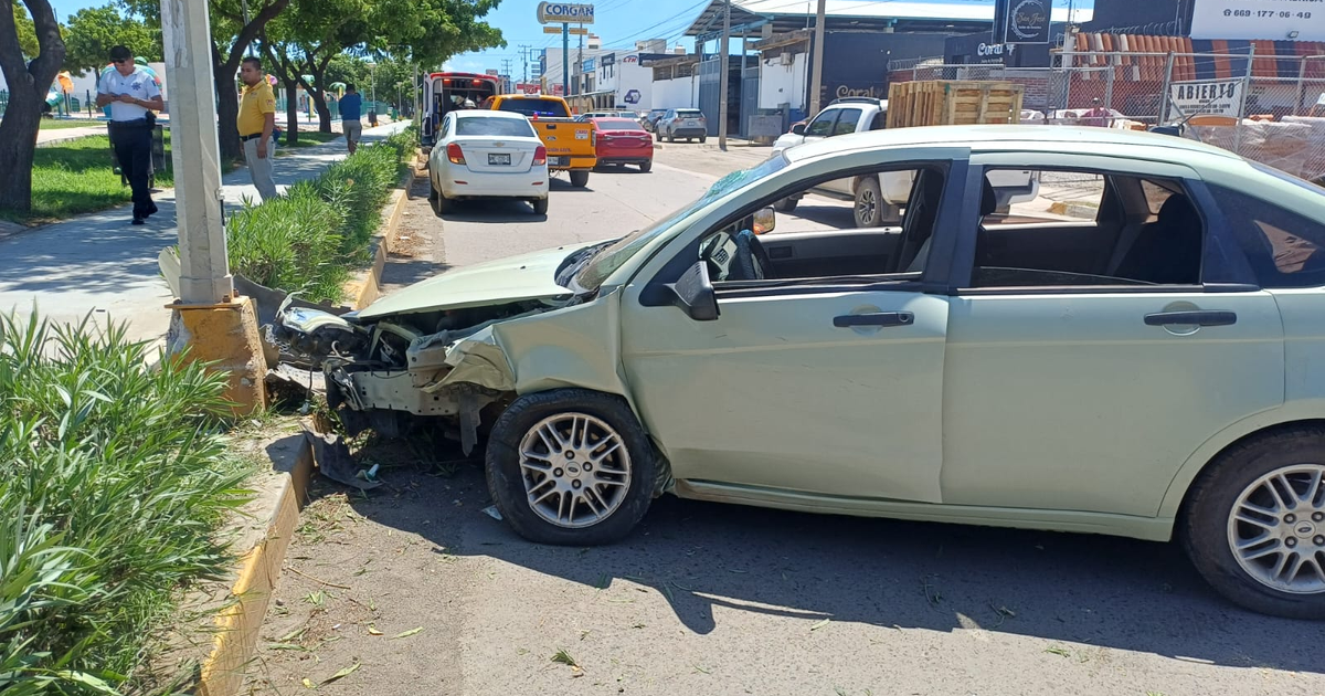 Automóvil verde chocado contra poste en Mazatlán, Sinaloa, con personas alrededor y otros vehículos en la carretera.