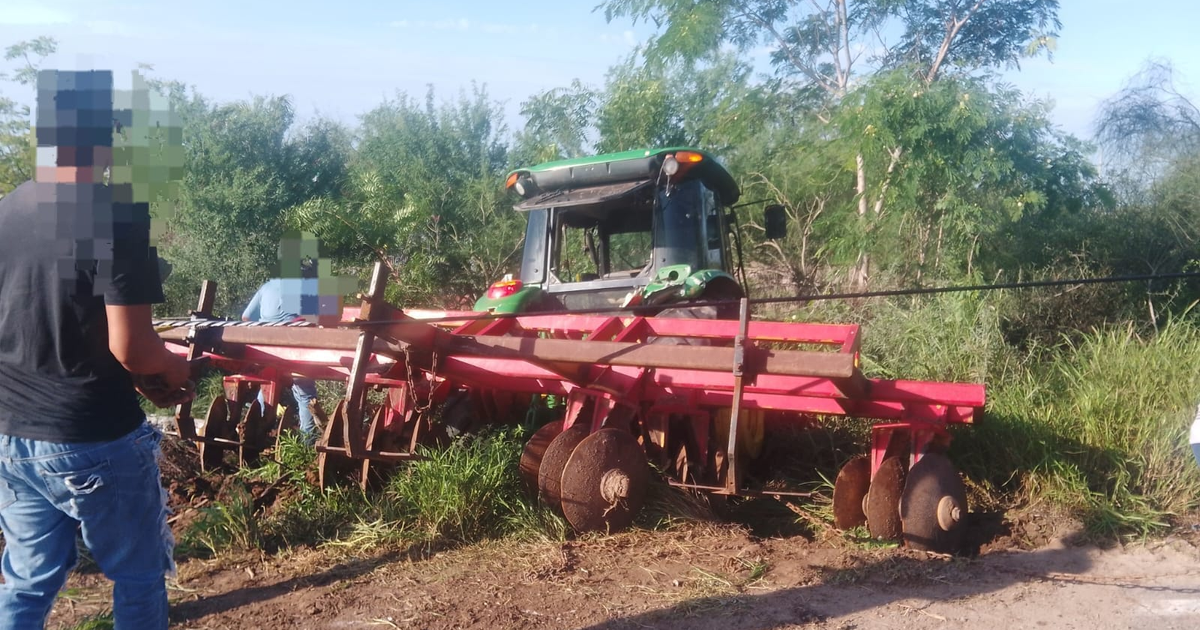Tractor agrícola con arado en un campo rural, operado por una persona, rodeado de vegetación y trabajadores.