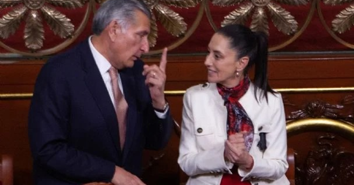 Dos personas conversando en un evento formal, una señalando y otra aplaudiendo, en un edificio gubernamental.