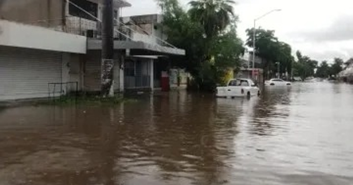Calle inundada en Ahome, Sinaloa, con vehículos sumergidos y edificios a los lados.