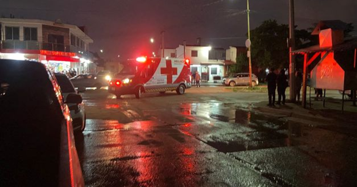 Ambulancia con luces intermitentes en una calle mojada de Culiacán durante la noche, con personas alrededor.