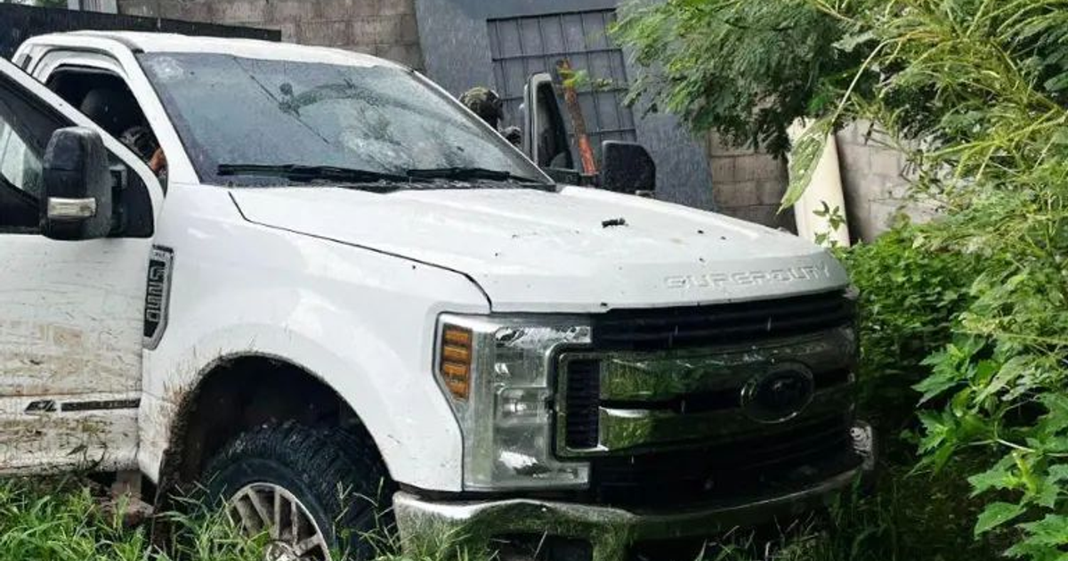 Camioneta Ford Súper Duty blanca con blindaje artesanal y puertas abiertas en un predio baldío.