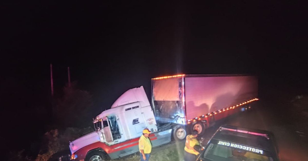 Camión de carga aparcado fuera de la carretera con luces encendidas, rodeado de trabajadores y un vehículo de seguridad, en un accidente nocturno en Sinaloa.