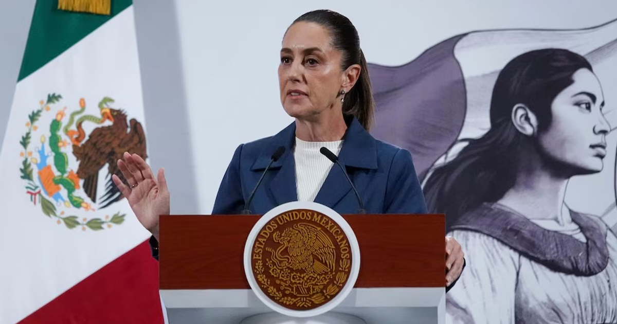 Claudia Sheinbaum en conferencia de prensa con bandera de México de fondo