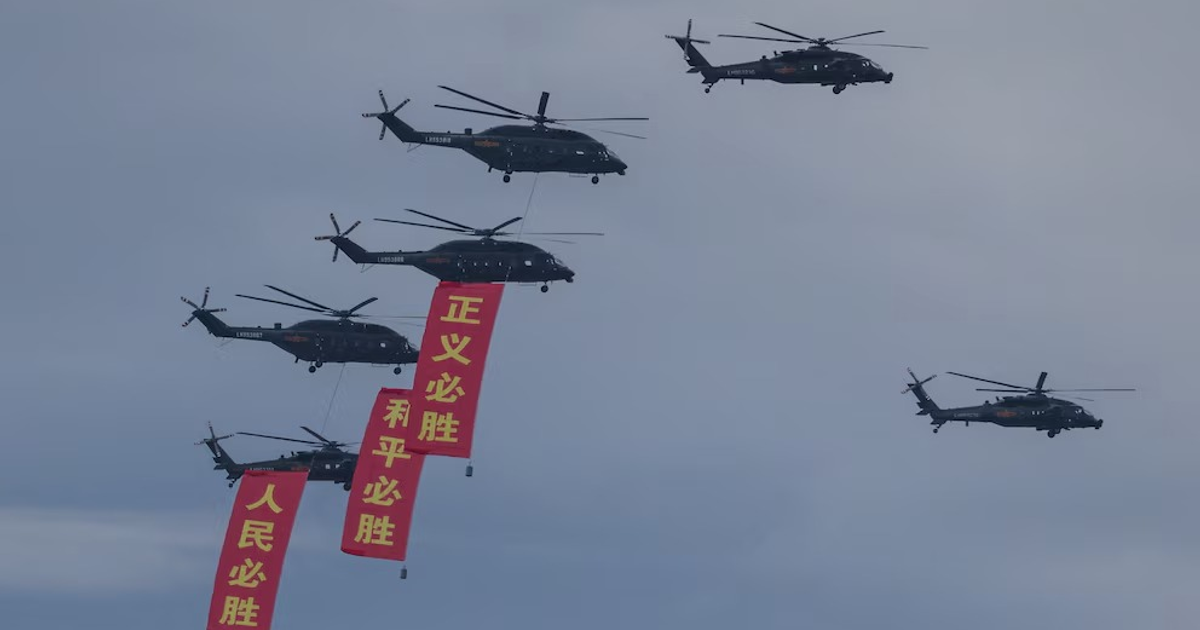 Helicópteros en formación con pancartas chinas sobre un cielo nublado durante el desfile militar en Beijing.