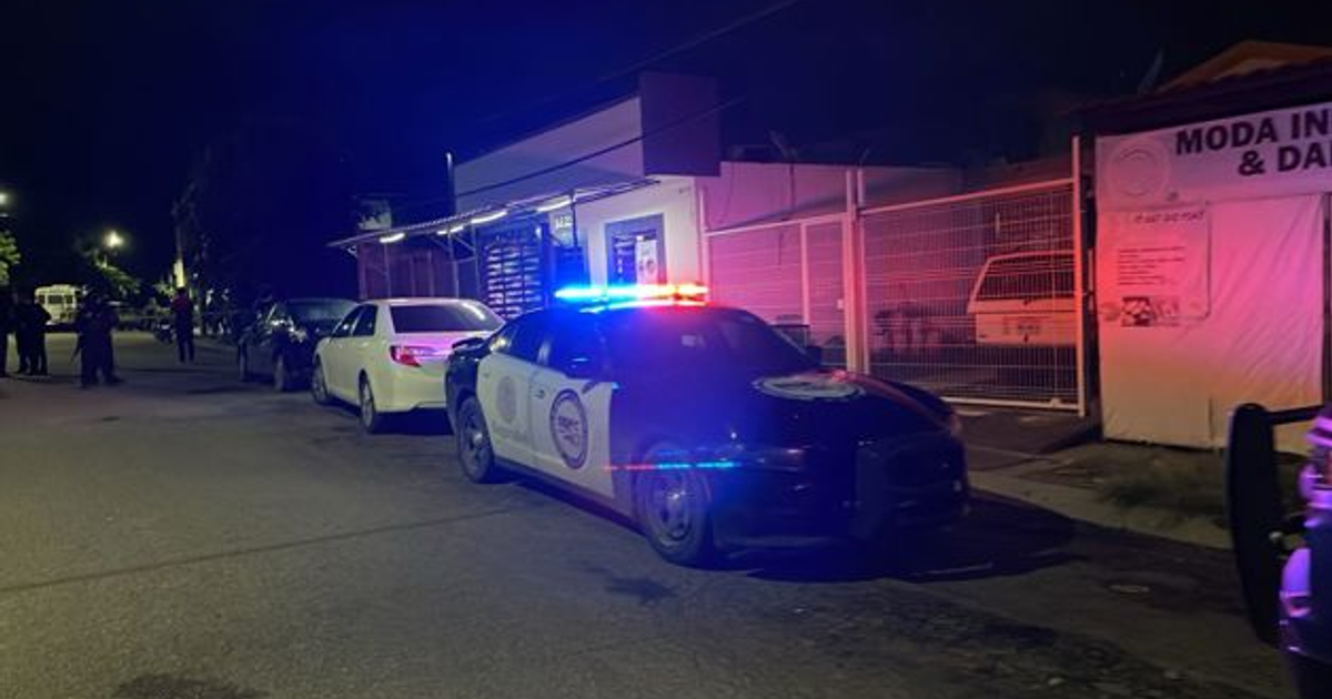 Calle nocturna en Culiacán con auto de policía y tienda 'MODA IN'