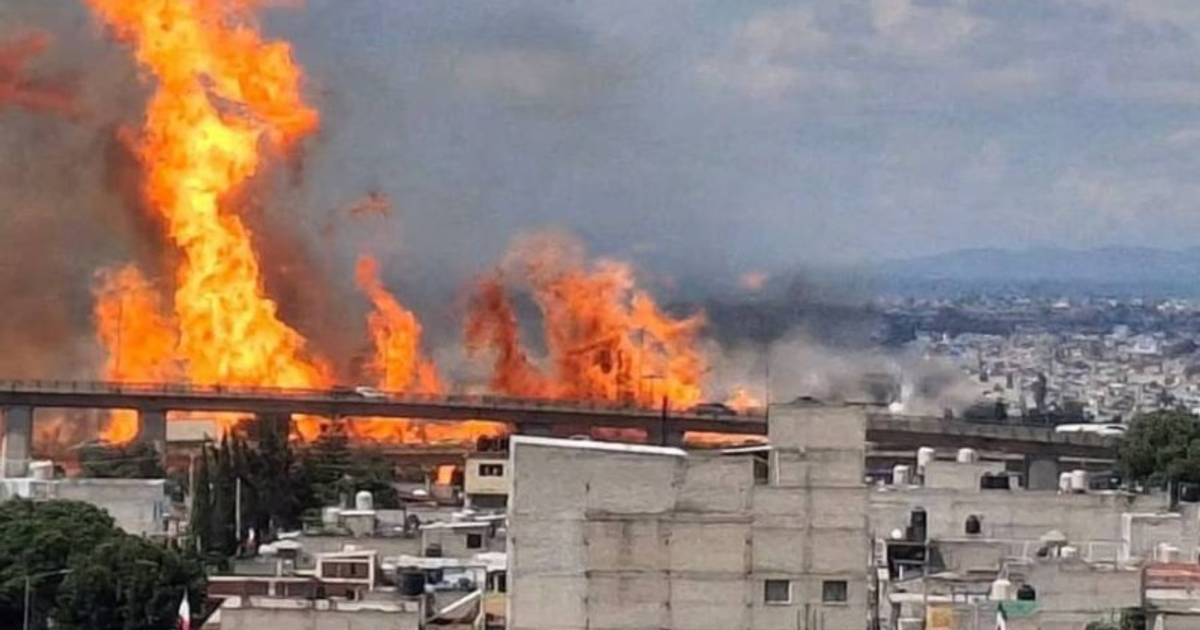 Incendio en Iztapalapa por explosión de pipa de gas LP, con llamas y humo visibles, puente y edificios al fondo.