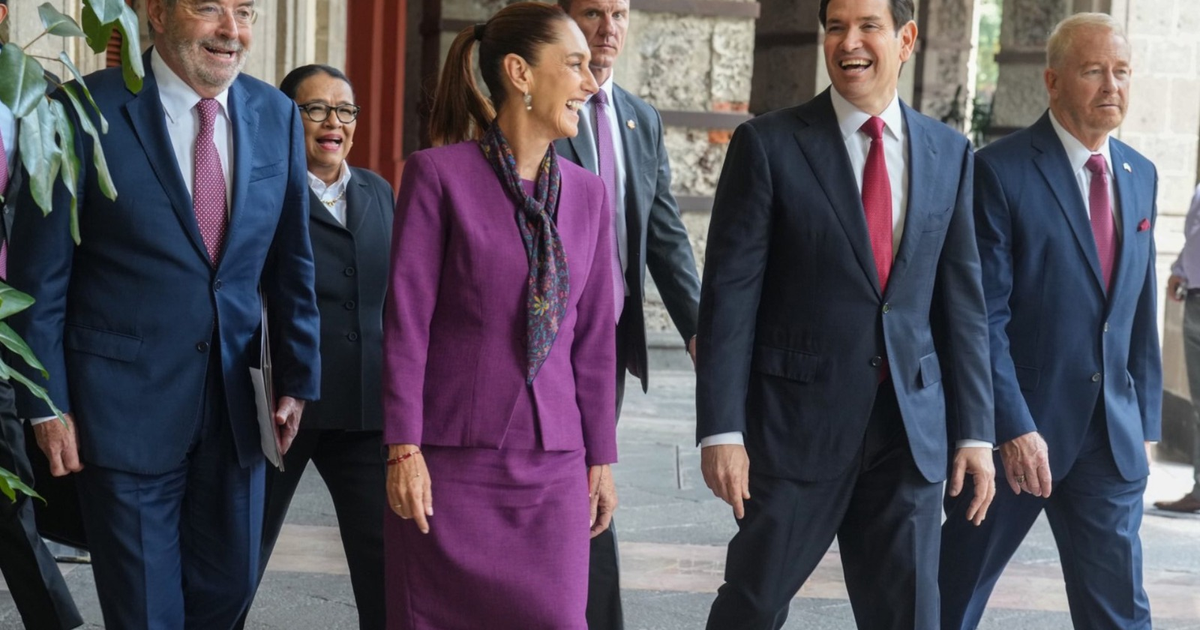 Grupo de personas vestidas formalmente conversando en un edificio gubernamental, con plantas decorativas en primer plano.