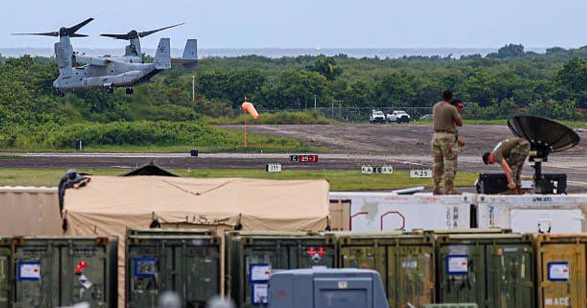 Helicóptero militar volando sobre base en Ceiba, Puerto Rico, con personal y contenedores en primer plano.