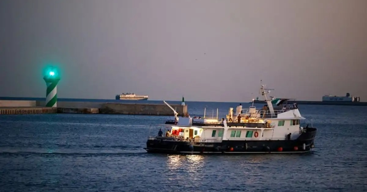 Barco navegando al atardecer con faro verde y otro barco en la distancia, cerca de Creta.