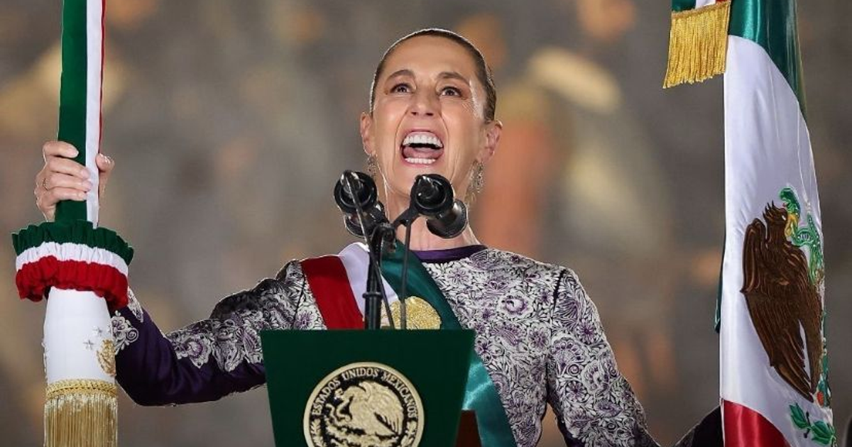 Claudia Sheinbaum pronuncia el Grito de Independencia en el Zócalo, sosteniendo un estandarte y una bandera de México.