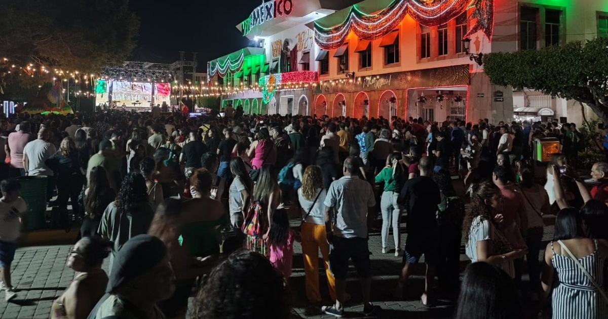 Multitud celebrando el Grito de Independencia en Mazatlán con escenario iluminado y adornos tricolores.