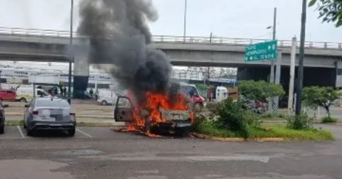 Vehículo en llamas en estacionamiento de Mazatlán, con humo negro y bomberos trabajando para controlar el incendio.