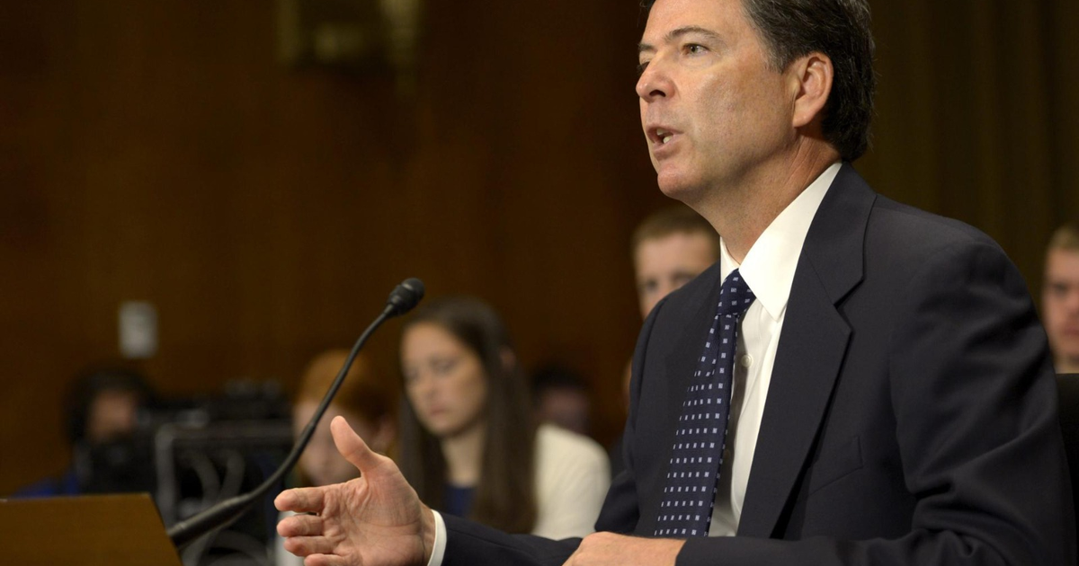James B. Comey testificando en un tribunal, vestido con traje oscuro y corbata, con personas al fondo prestando atención.