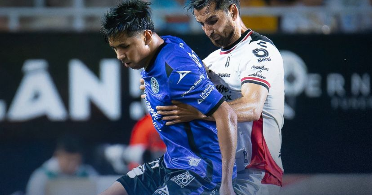 Dos jugadores de fútbol en acción durante el Clásico de Clásicos de la Jornada 8 del Apertura 2025, uno con camiseta azul y otro con camiseta blanca con detalles en rojo, en un estadio.