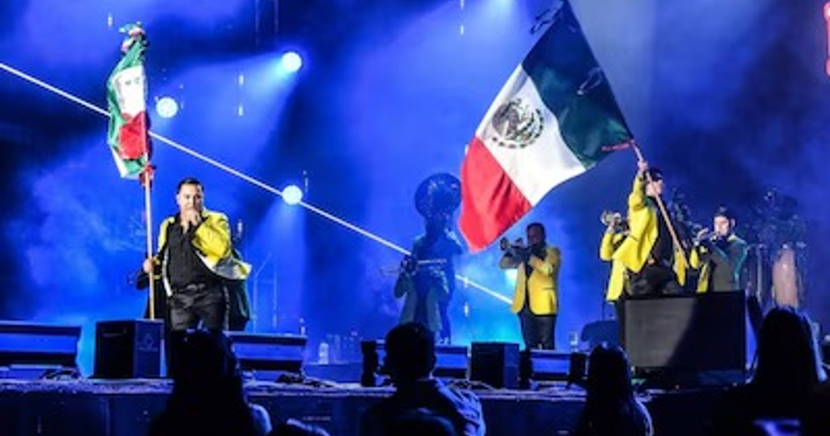 Artista de La Arrolladora Banda El Limón con bandera de México en el Zócalo