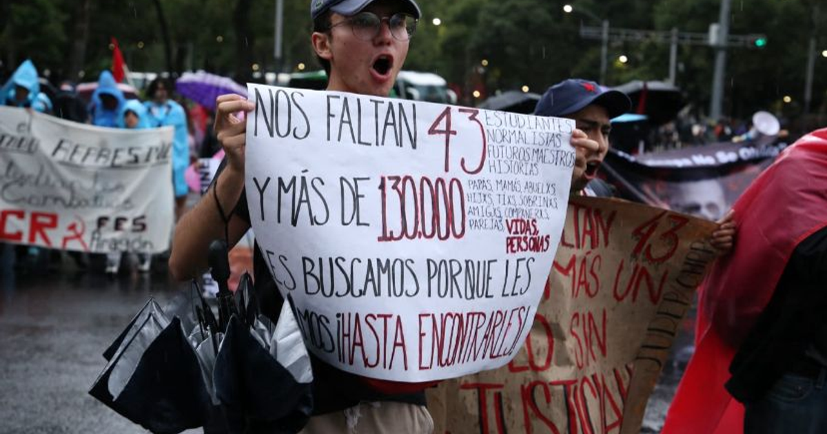 Manifestantes en Ciudad de México exigiendo justicia por los 43 estudiantes de Ayotzinapa, con pancartas y paraguas bajo la lluvia.