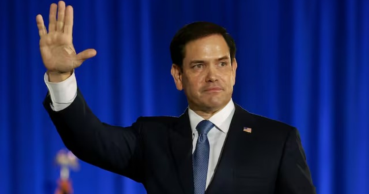 Persona saludando en evento con cortinas azules, relacionado con la visita de Marco Rubio a México.
