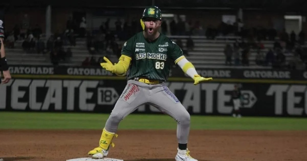 Jugador de béisbol celebrando en el campo con uniforme verde y gris, manos levantadas y expresión de júbilo.
