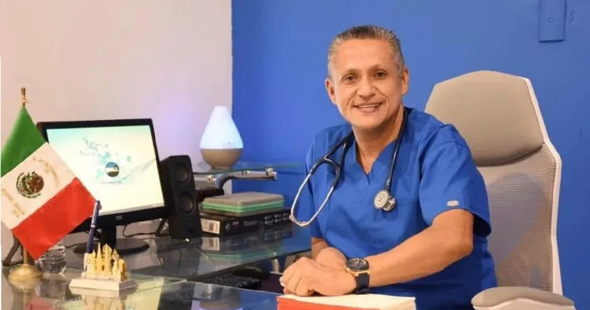 Médico sonriente en oficina con bandera de México y estetoscopio