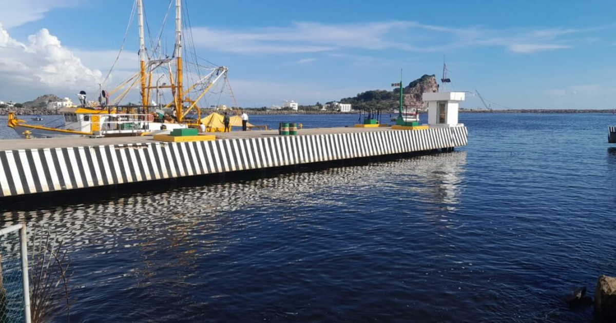 Muelle de Mazatlán con el barco camaronero 'Doña Luz' anclado, trabajadores presentes y paisaje de fondo.