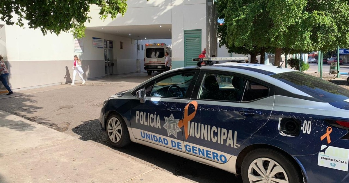 Vehículo de la Unidad de Género de la Policía Municipal frente a un hospital con ambulancia en acción.