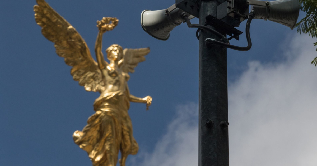 Escultura dorada de ángel con corona y poste con altavoces bajo cielo azul, en contexto de sismos en México.
