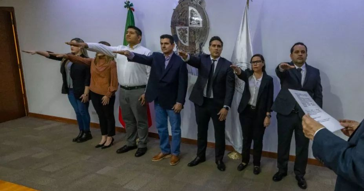Grupo de funcionarios de Sinaloa rindiendo protesta, levantando la mano derecha, con banderas y escudo de fondo.