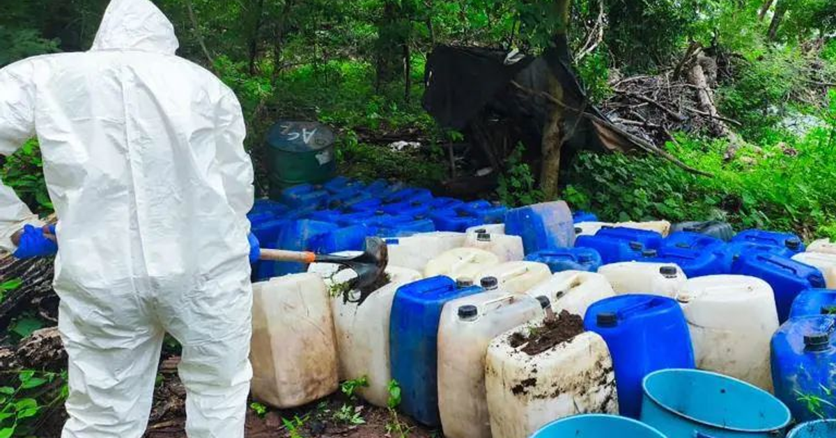 Soldado en traje de protección manipulando tierra cerca de contenedores plásticos en un operativo contra precursores químicos en Culiacán.