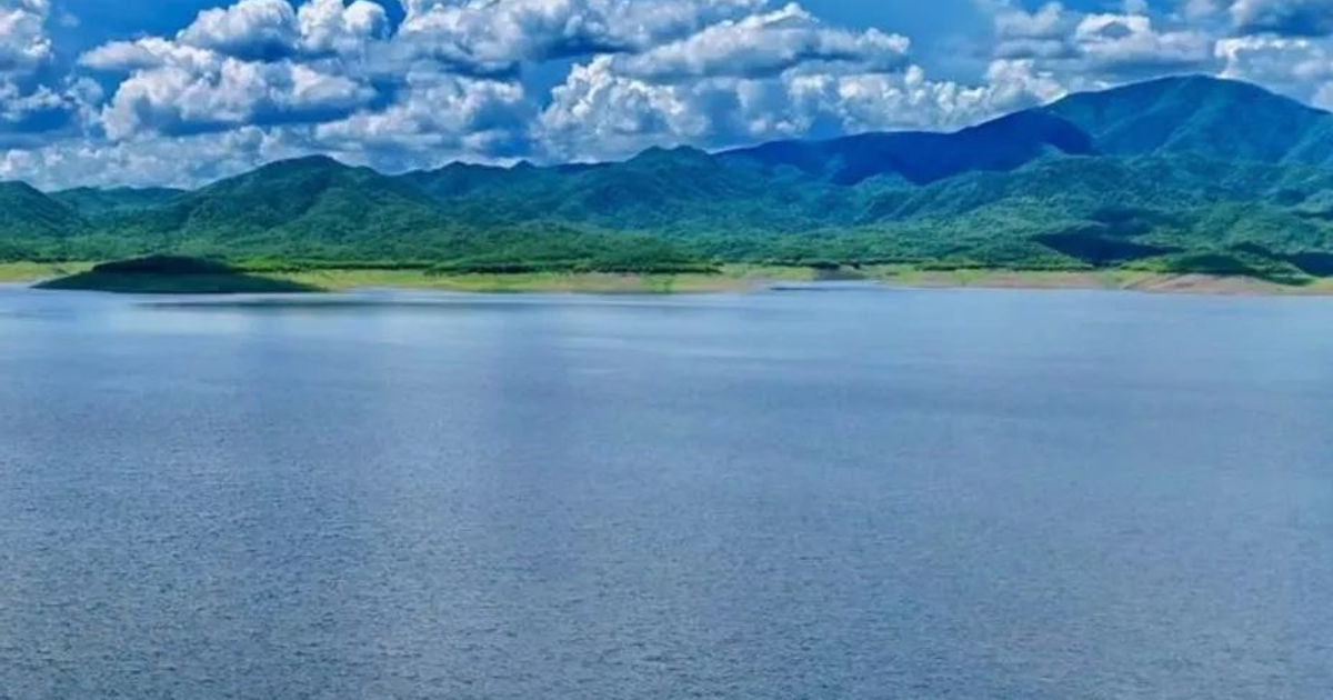 Lago en primer plano con montañas al fondo y cielo despejado, representando la naturaleza de Sinaloa.