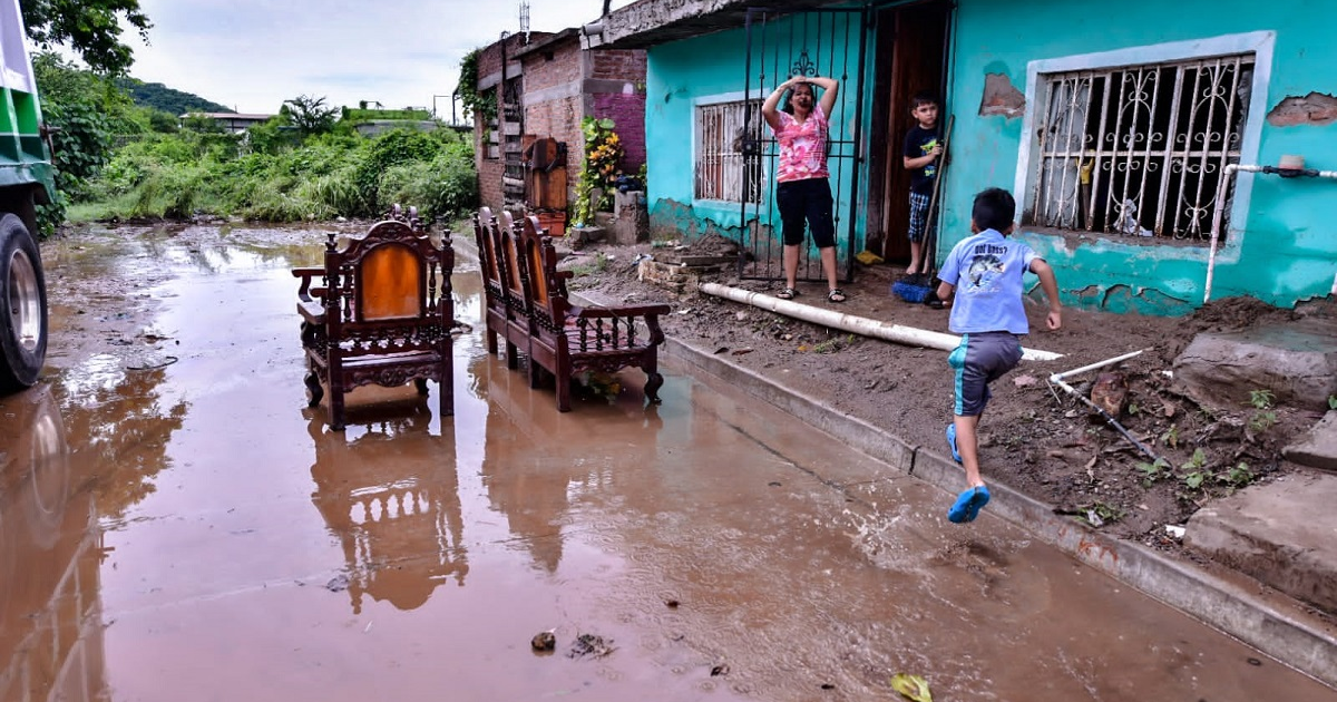Calle inundada en Culiacán con muebles y personas afectadas por la tormenta 'Lorena'.