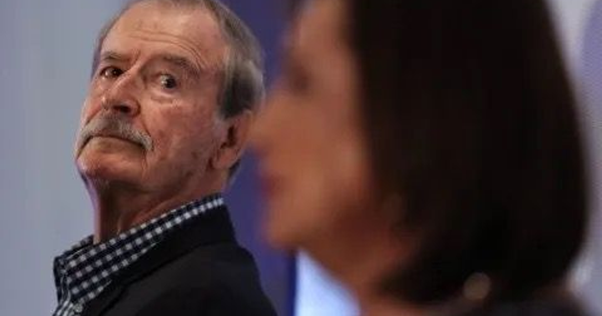Dos personas en un evento, una mirando hacia atrás y otra desenfocada, vinculadas a declaraciones de Vicente Fox sobre salario mínimo.