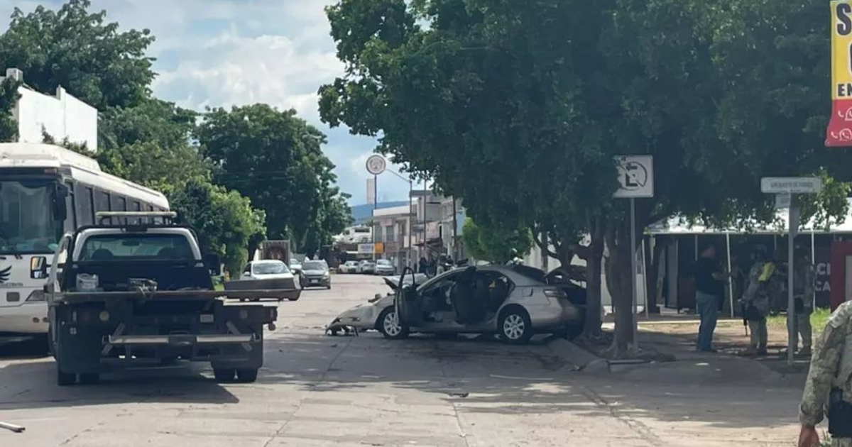 Vehículo gris estacionado en la acera en una calle de Culiacán, con personas discutiendo cerca.