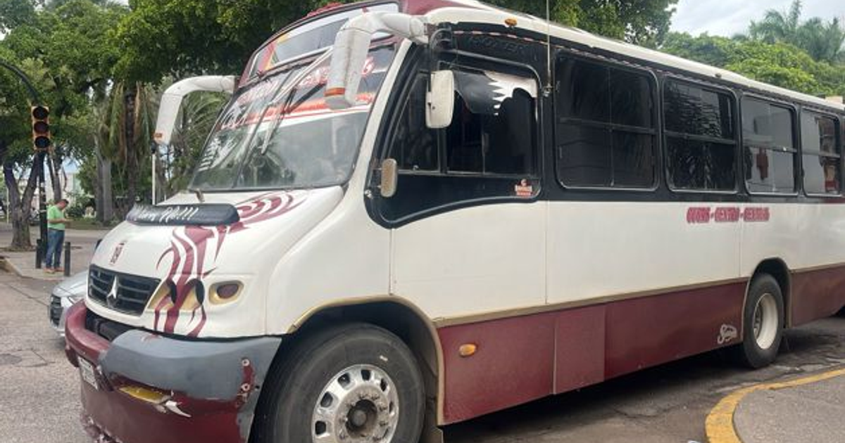 Autobús de transporte público en Culiacán con detalles en rojo, detenido en una calle con semáforos y árboles de fondo.