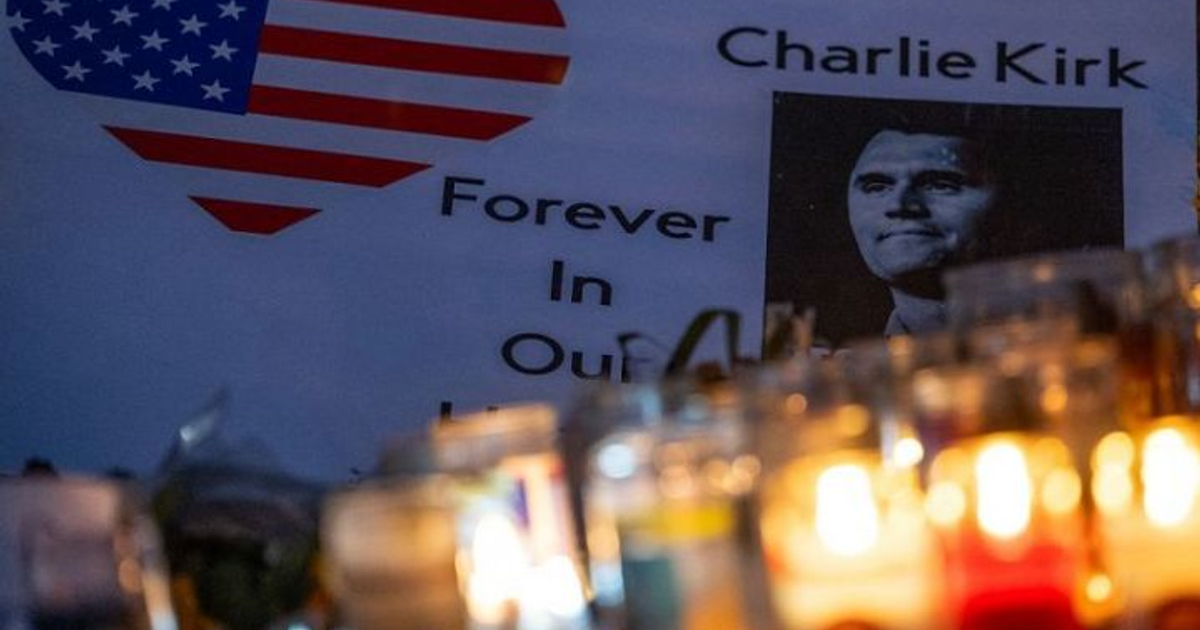 Cartel con 'Forever In Our Hearts' y foto de Charlie Kirk en memorial con velas encendidas.