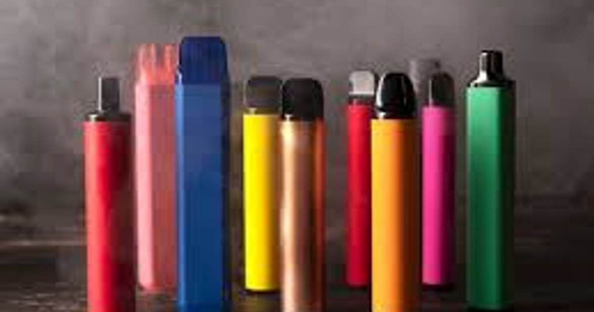 Varios dispositivos de vapeo de diferentes colores y tamaños sobre una superficie oscura con fondo vaporoso.