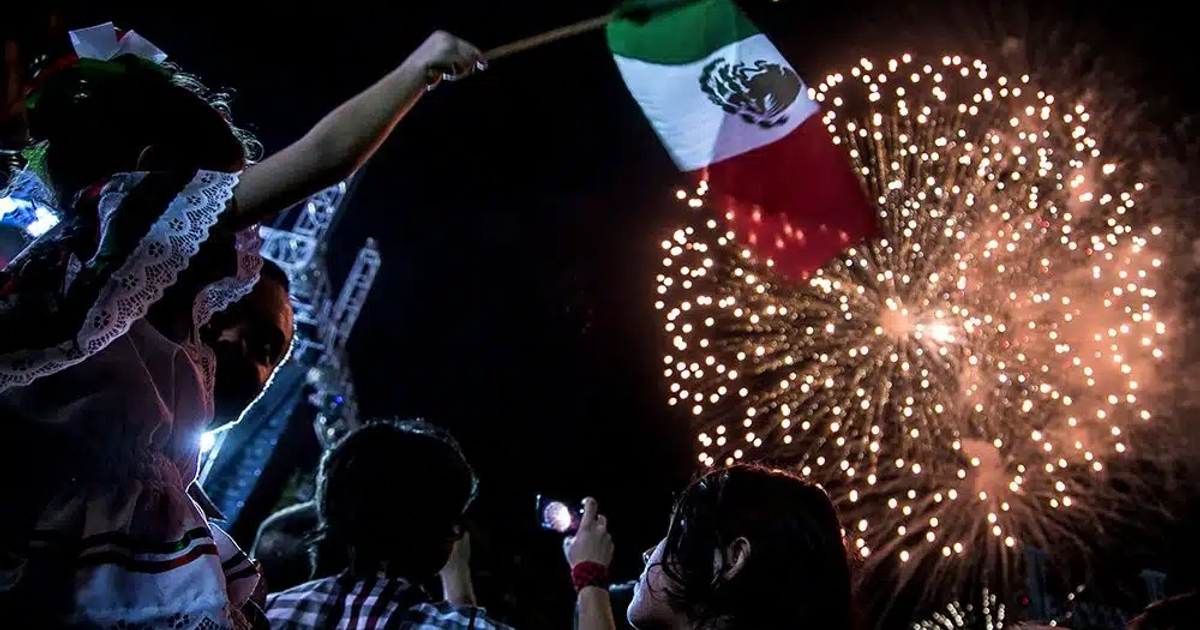 Fuegos artificiales y celebración del Grito de Independencia en Sinaloa, México, con una niña sosteniendo una bandera mexicana.