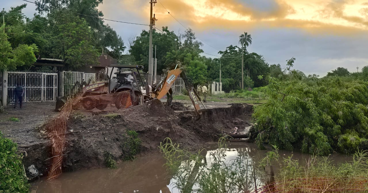 Excavadora trabajando en reparación del dren San Joachín, Guasave, con cercado de seguridad y vegetación alrededor.