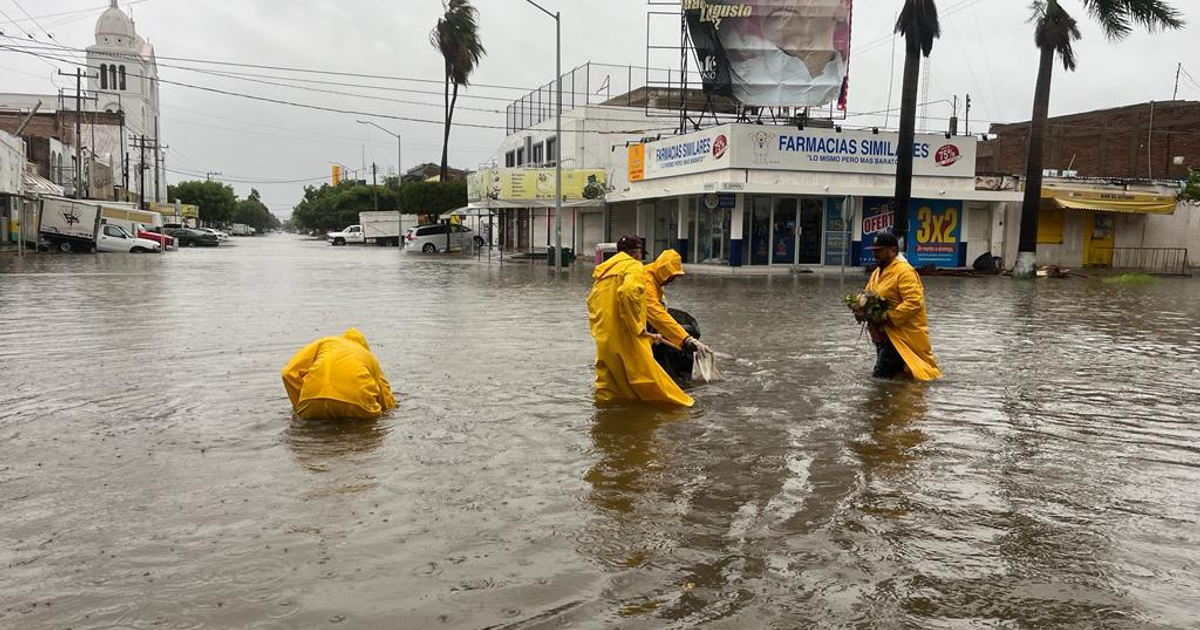 Personas con impermeables amarillos en una calle inundada en Los Mochis, Sinaloa, tras tormenta tropical Lorena.