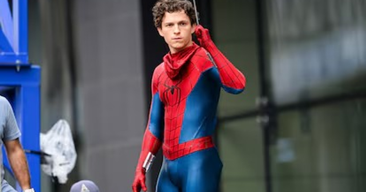 Persona vestida como Spider-Man en una escena de filmación urbana, con un miembro del equipo de producción al fondo.