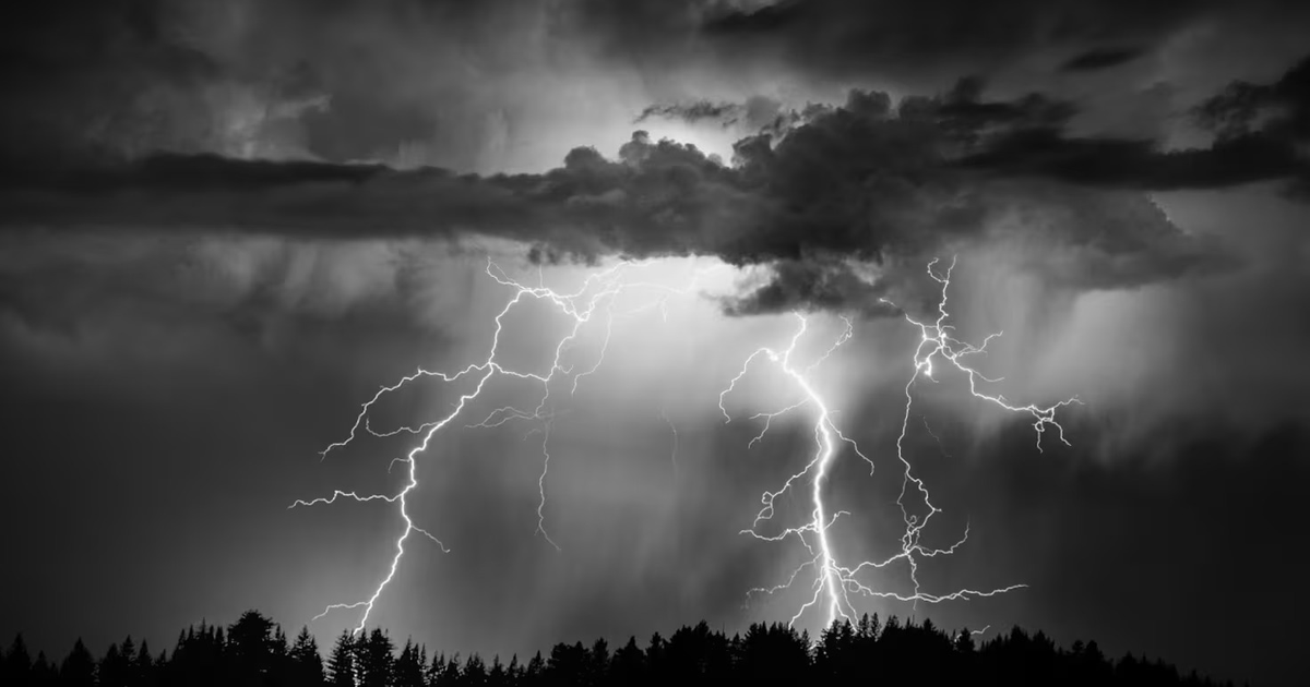 Cielo nublado con relámpagos y siluetas de árboles durante una tormenta eléctrica.