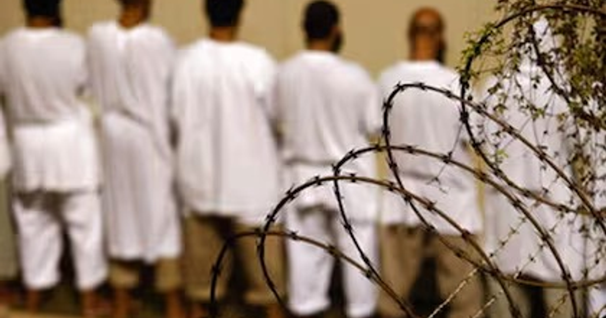 Personas con túnicas blancas frente a una valla de alambre de púas, simbolizando restricción en prisiones cubanas.