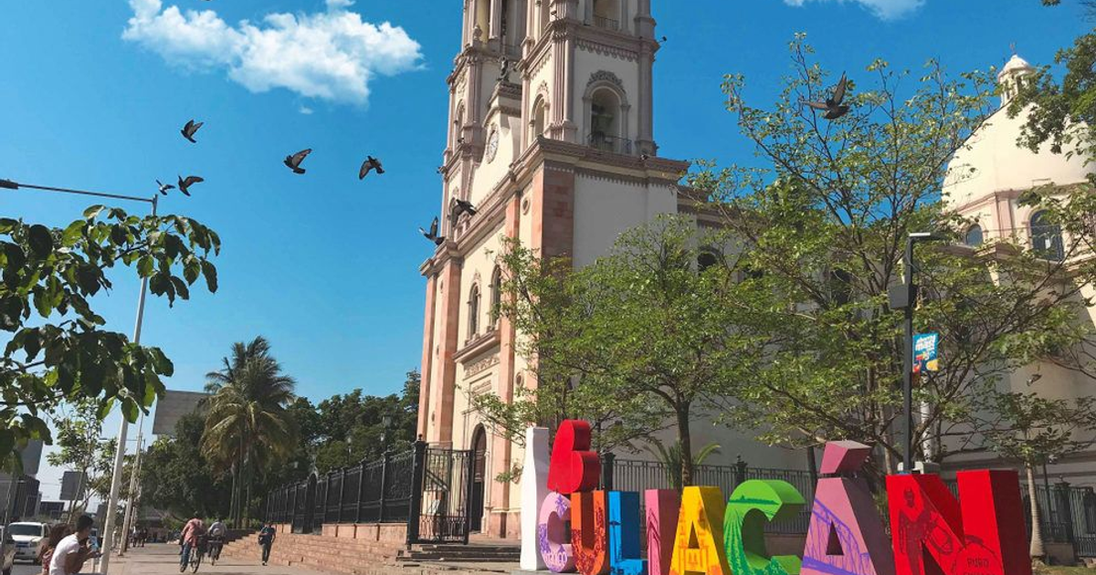 Plaza central de Culiacán con iglesia y estructura colorida, cielo azul y aves volando.