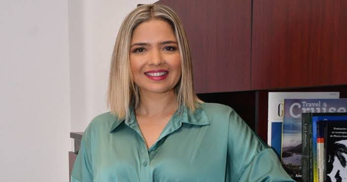Persona con cabello corto y camisa verde sonriendo frente a estantería de libros