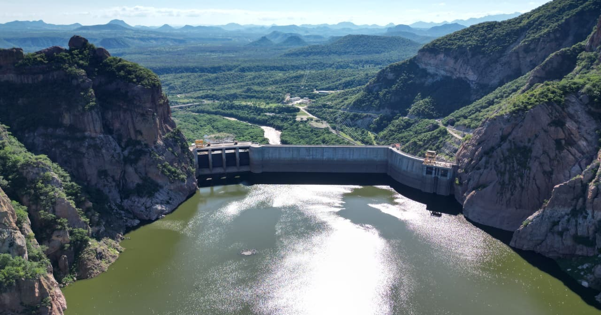 Vista de un embalse y presa en un entorno montañoso en Sinaloa, con vegetación y caminos visibles.