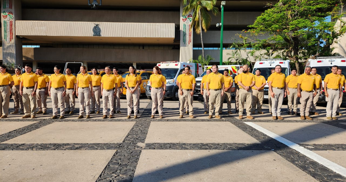 Grupo de personas con camisetas amarillas en evento de homenaje a la Protección Civil en Culiacán, con vehículos de emergencia al fondo.