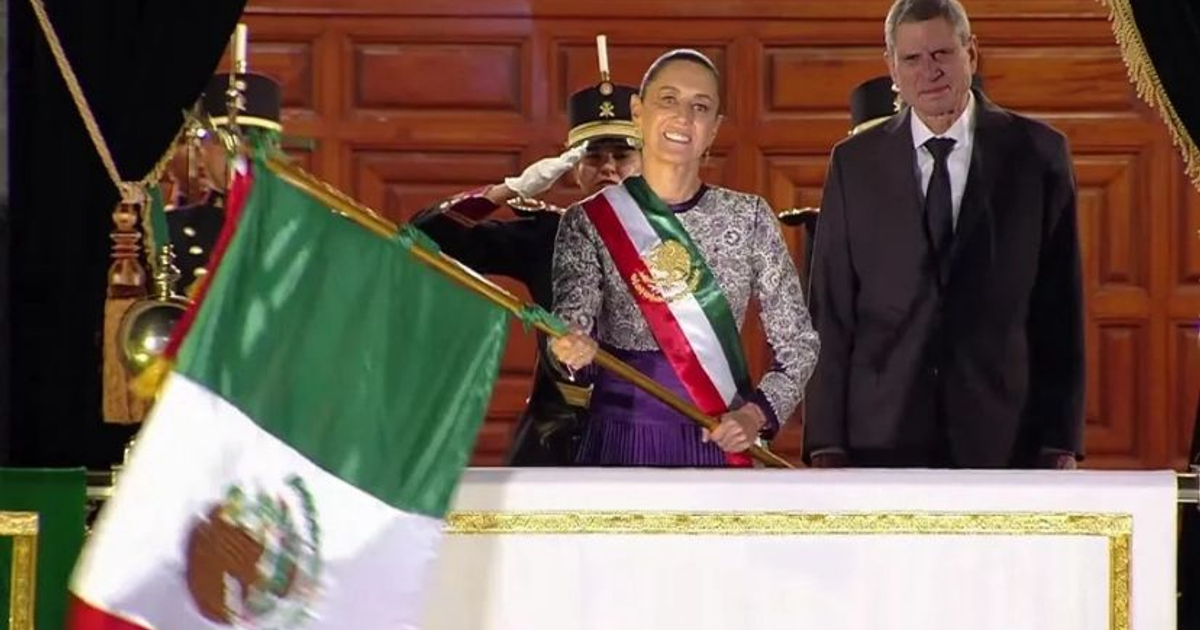 Mujer con bandera de México en el Grito de Independencia, junto a un hombre en traje oscuro.
