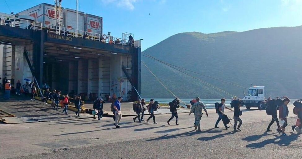 Personas descendiendo de un barco en un puerto de Sinaloa, con un hombre en uniforme militar presente.