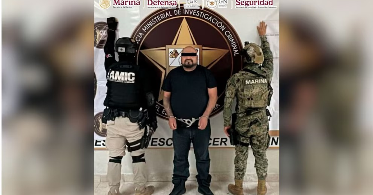 Hombre esposado flanqueado por fuerzas de seguridad en presentación oficial