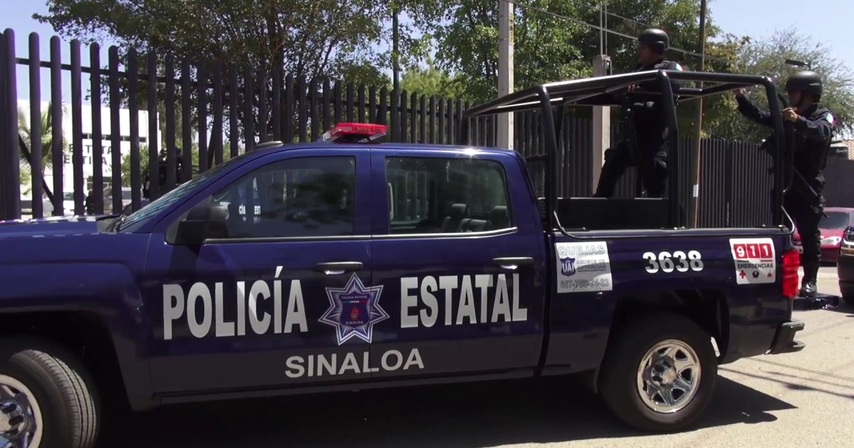 Camioneta azul de la Policía Estatal de Sinaloa con dos oficiales en la parte trasera en un entorno urbano.